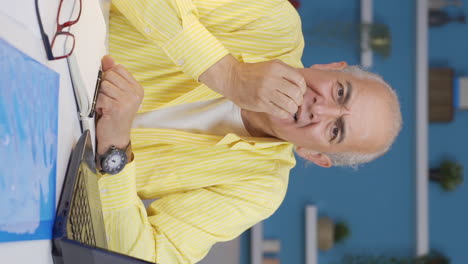 Vertical-video-of-Home-office-worker-old-man-biting-his-nails-looking-at-camera.